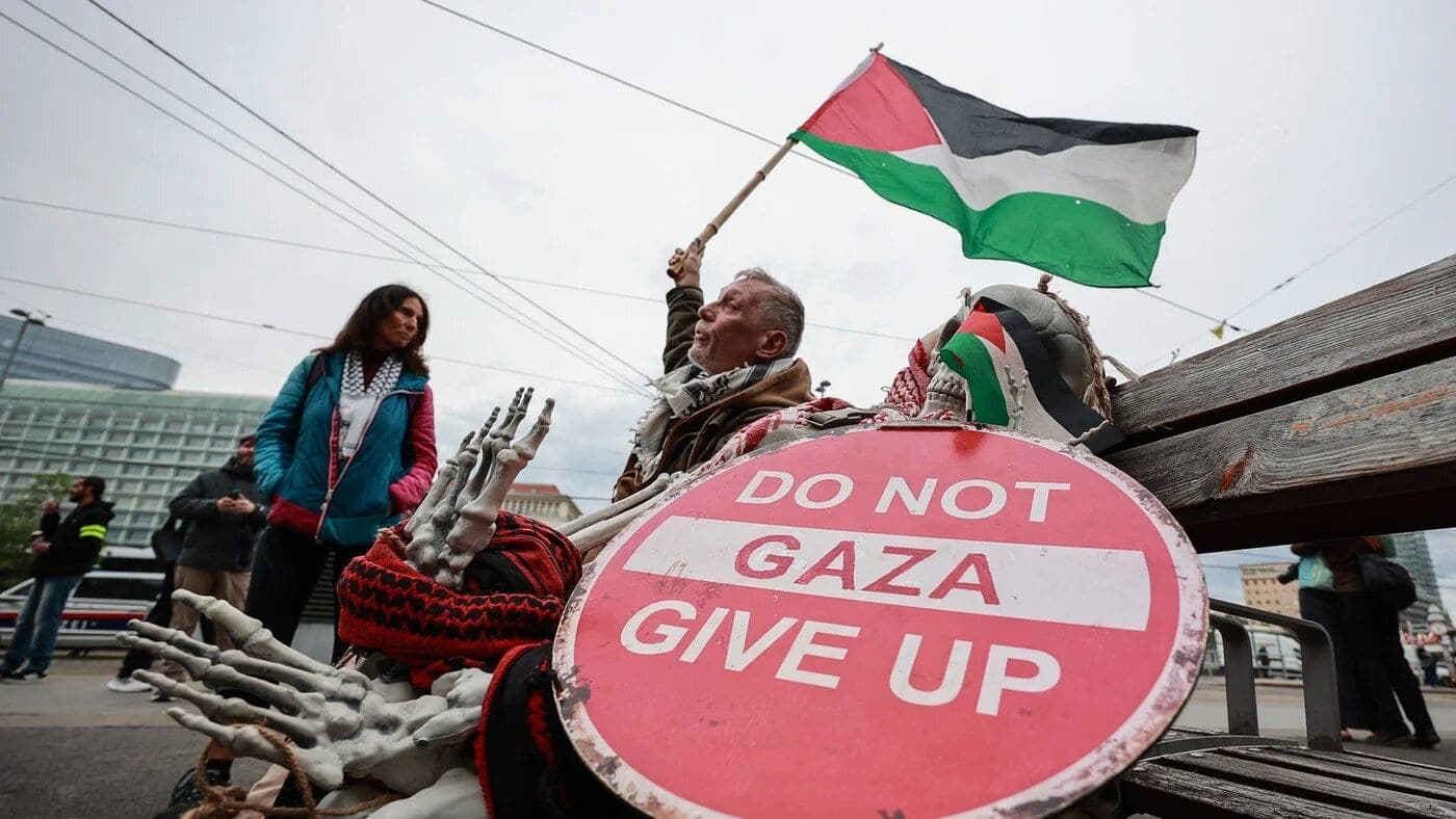 A man holds a Palestinian flag beside a sign reading "Do not give up Gaza" during a protest in Vienna on 12 May 2026 (Radek Mica/AFP)