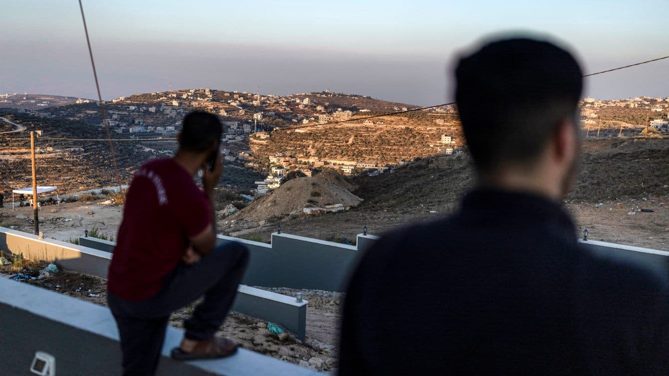 Palestinian men watch Israeli soldiers from the roof of a home besieged by settlers in Qusra, occupied West Bank, 18 August 2026 (Ilia Yefimovich/AFP)